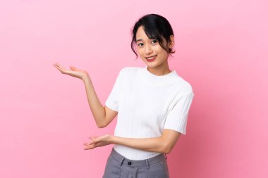 Pembe arka planda izole edilmiş genç Vietnamlı kadın davet edilmek için ellerini yana uzatıyor.