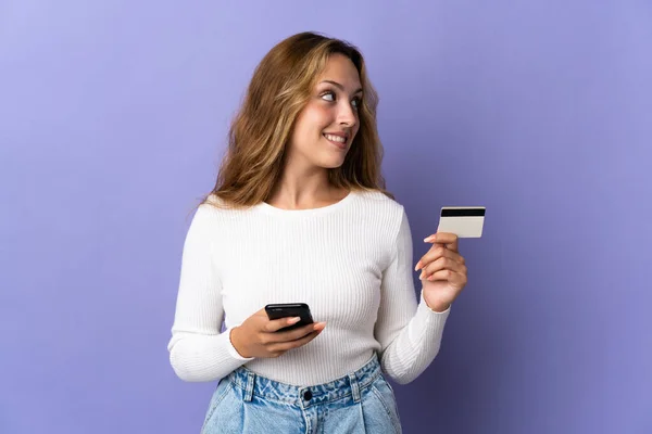 Jonge Blonde Vrouw Geïsoleerd Paarse Achtergrond Kopen Met Mobiele Telefoon — Stockfoto