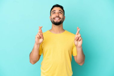 Genç Arap adam mavi arka planda izole edilmiş, şans diliyor ve en iyisini diliyor.