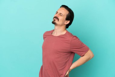 Genç beyaz adam mavi arka planda izole edildi. Çaba sarfettiği için sırt ağrısı çekiyor.