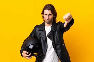 Motosiklet kasklı bir adam sarı arka planda izole edilmiş, olumsuz ifadeli baş parmağını gösteriyor.