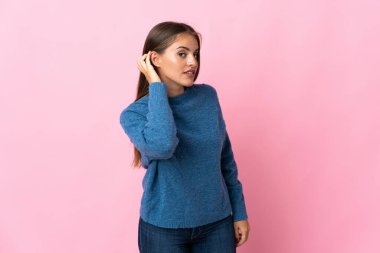 Genç Uruguaylı kadın pembe arka planda izole edilmiş bir şekilde elini kulağına koyarak bir şeyler dinliyor.