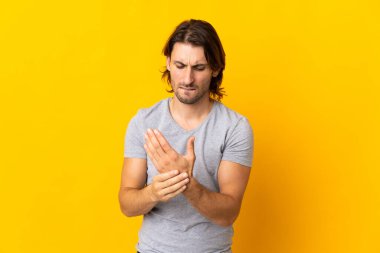Sarı arka planda izole edilmiş genç yakışıklı ellerinde acıdan kıvranıyor.