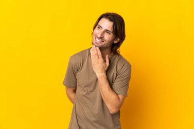 Sarı arka planda izole edilmiş genç yakışıklı adam gülümserken yukarı bakıyor.