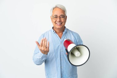 Middle age Brazilian man isolated on white background holding a megaphone and inviting to come with hand