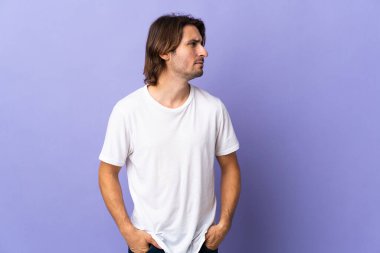 Mor arka planda soyutlanmış genç yakışıklı adam yan tarafa bakıyor.
