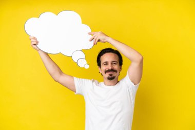 Sarı arka planda izole edilmiş genç beyaz bir adam düşünme balonu tutuyor.
