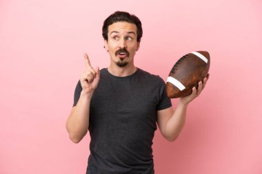 Genç beyaz adam rugby oynuyor. Pembe arka planda izole edilmiş. Parmakla işaret eden bir fikir düşünüyor.