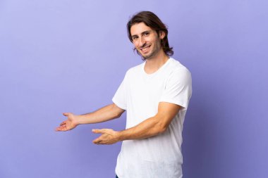 Mor arka planda soyutlanmış genç yakışıklı adam, davet edilmek için ellerini yana uzatıyor.