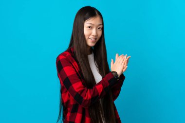 Genç Çinli kız, izole edilmiş mavi arka planı alkışlıyor.