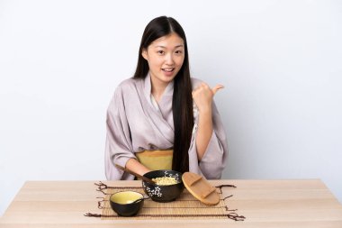 Kimono giyen ve erişte yiyen genç bir Çinli kız bir ürün sunmak için kenarı işaret ediyor.