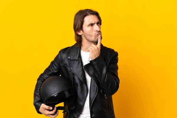 見上げながら疑問を持ちながら黄色の背景に隔離されたオートバイのヘルメットを持つ男 — ストック写真