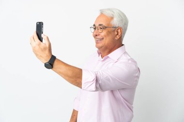 Orta yaşlı Brezilyalı adam beyaz arka planda izole edilmiş cep telefonuyla selfie çekiyor.