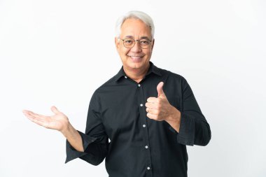 Middle age Brazilian man isolated on white background holding copyspace imaginary on the palm to insert an ad and with thumbs up