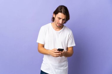 Mor arka planda izole edilmiş genç bir adam cep telefonuyla mesaj gönderiyor.