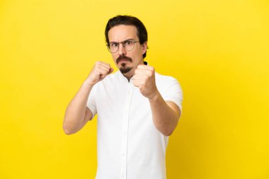 Kafkasyalı genç adam sarı arka planda yalıtılmış bir şekilde dövüşüyor.