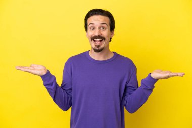 Sarı arka planda izole edilmiş genç beyaz adam şok olmuş yüz ifadesi ile