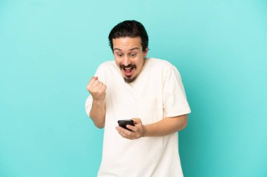 Mavi arka planda izole edilmiş genç beyaz adam şaşırdı ve bir mesaj gönderiyor.