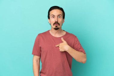 Mavi arka planda izole edilmiş genç beyaz adam kendini işaret ediyor.
