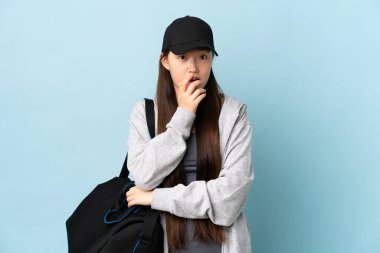 Spor çantasıyla gezen genç Çinli kadın mavi arka planda, sağa bakarken şaşırmış ve şok olmuştu.