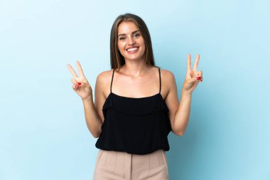 Mavi arka planda izole edilmiş genç Uruguaylı kadın iki eliyle zafer işareti gösteriyor.