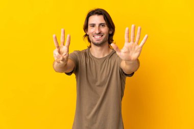 Sarı arka planda izole edilmiş genç yakışıklı sekiz parmaklı sayıyor