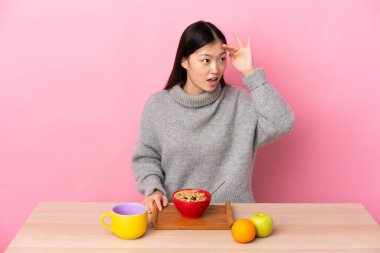 Genç Çinli bir kız, yan bakarken sürpriz bir ifadeyle kahvaltı yapıyor.