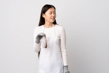 Çinli balıkçı önlük takıyor ve yalıtılmış beyaz arka planda çiğ balık tutuyor. Yana bakıyor ve gülümsüyor.