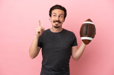 Genç beyaz adam pembe arka planda izole edilmiş rugby oynuyor. Harika bir fikre işaret ediyor.