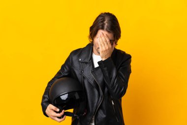 Motosiklet kasklı bir adam sarı arka planda izole edilmiş, yorgun ve hasta bir yüz ifadesi var.