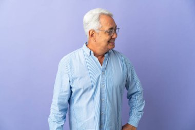 Mor arka planda izole edilmiş orta yaşlı Brezilyalı adam yana bakıyor ve gülümsüyor.