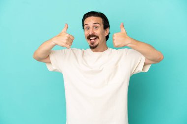 Kafkasyalı genç adam mavi arka planda izole edilmiş bir şekilde baş parmak işareti yapıyor.