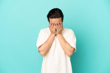 Kafkasyalı genç adam mavi arka planda izole edilmiş, yorgun ve hasta bir ifadeyle.