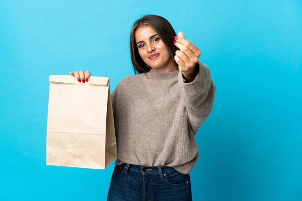 女人拿着一包蓝色背景的外卖食品做手势赚钱 — 图库照片