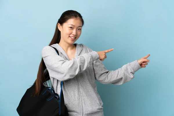 年轻的中国女运动员 背着运动包 背对着孤立的蓝色背景 手指指向侧面 并展示了一种产品 — 图库照片