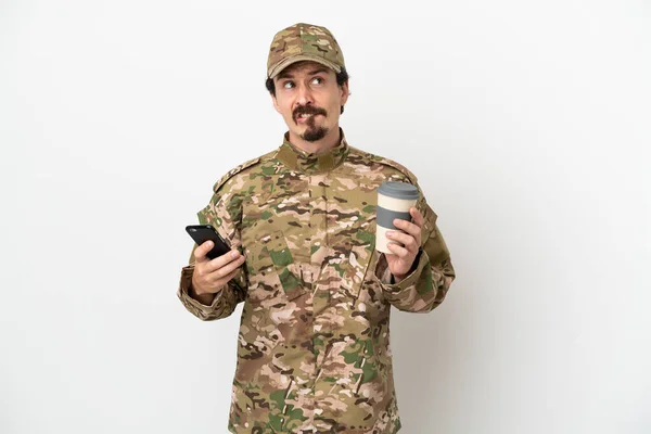 士兵被隔离在白色背景下 一边拿着咖啡 一边想着什么 一边拿着手机 — 图库照片