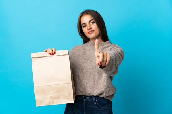 女人拿着一包外卖食品 蓝色背景下隔离 露出并举起一只手指头 — 图库照片