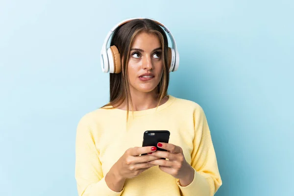 Young Uruguayan Woman Isolated Blue Background Listening Music Mobile Thinking — Foto de Stock