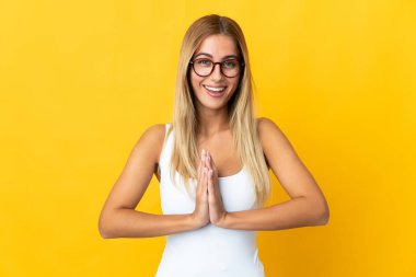 Sarı arka planda izole edilmiş genç sarışın kadın avuç içlerini bir arada tutuyor. İnsan bir şey ister.