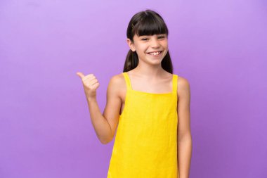 Mor arka planda izole edilmiş küçük beyaz çocuk bir ürünü sunmak için kenarı işaret ediyor.