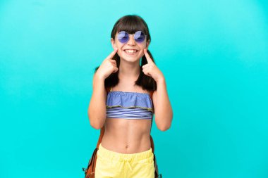 Küçük beyaz bir çocuk kumsala gidiyor mavi arka planda yalnız mutlu ve hoş bir ifadeyle gülümsüyor.