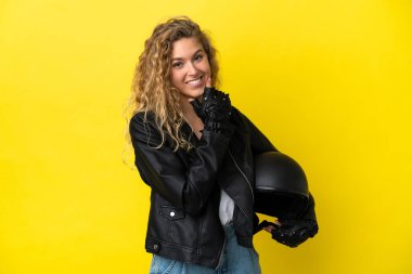Sarı arka planda izole edilmiş motosiklet kasklı genç sarışın kadın mutlu ve gülümsüyor.
