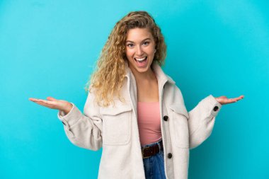 Genç sarışın kadın mavi arka planda izole edilmiş, şok olmuş yüz ifadesi var.