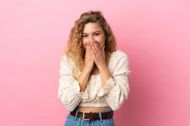 Pembe arka planda izole edilmiş genç sarışın kadın mutlu ve gülümsüyor elleriyle ağzını kapatıyor.