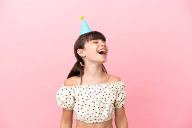 Doğumgünü şapkalı küçük beyaz çocuk pembe arka planda izole edilmiş gülüyor.