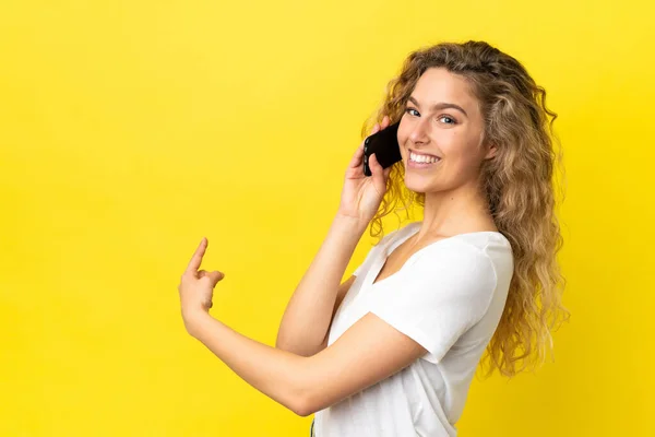 Молодая Блондинка Помощью Мобильного Телефона Изолированы Желтом Фоне Указывая Назад — стоковое фото