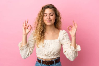 Zen pozisyonunda pembe arka planda izole edilmiş genç sarışın kadın.