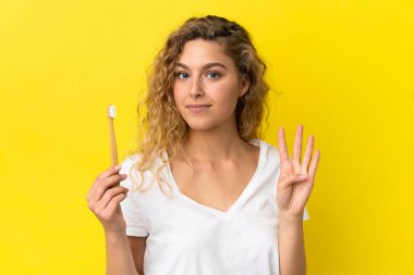 Sarı arka planda dişlerini fırçalayan beyaz bir kadın mutlu ve parmakları olan dört kişi sayıyor.