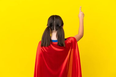 Mor arka planda izole edilmiş küçük süper kahraman çocuk işaret parmağıyla işaret ediyor.