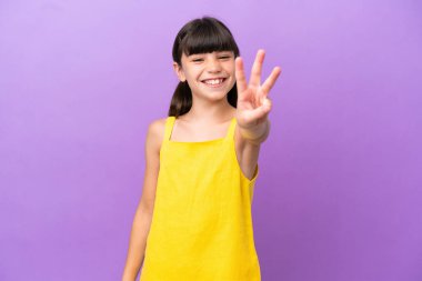 Küçük beyaz çocuk mor arka planda izole edilmiş mutlu ve parmaklarıyla üçe kadar sayıyor.
